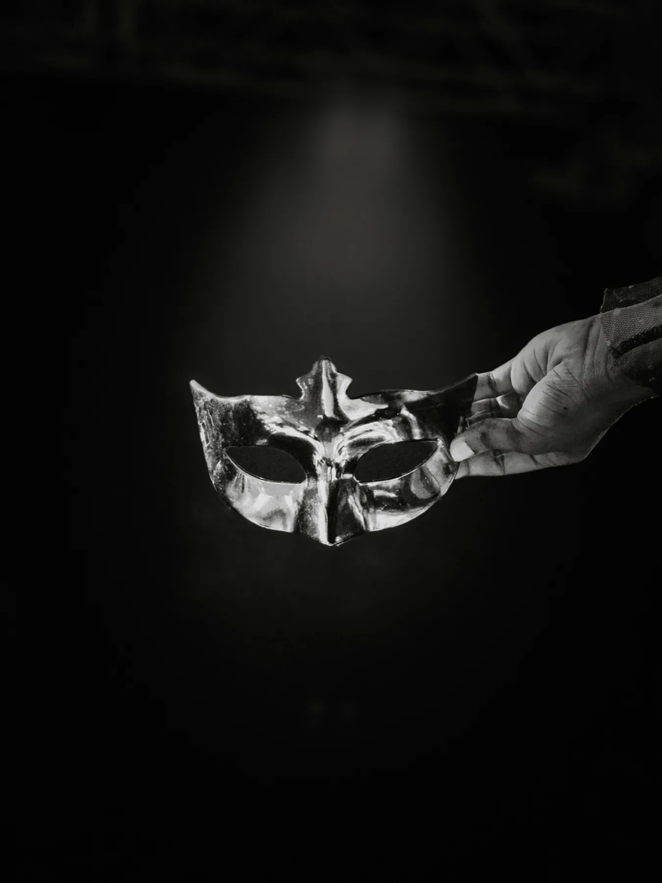 Une main tient un masque de bal argenté, en noir et blanc